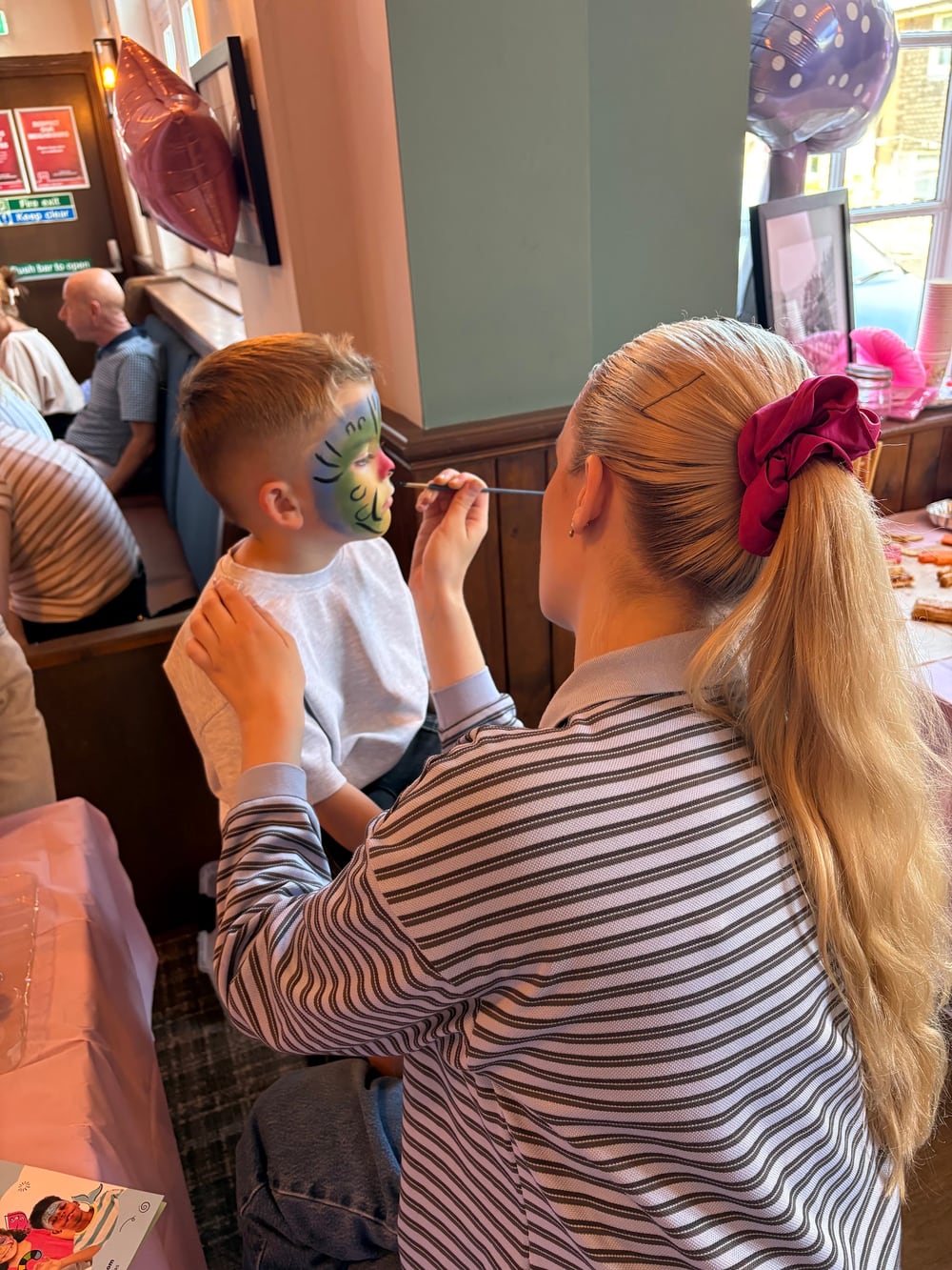 Ellie adding the finishing touches to a child's face paint at a party